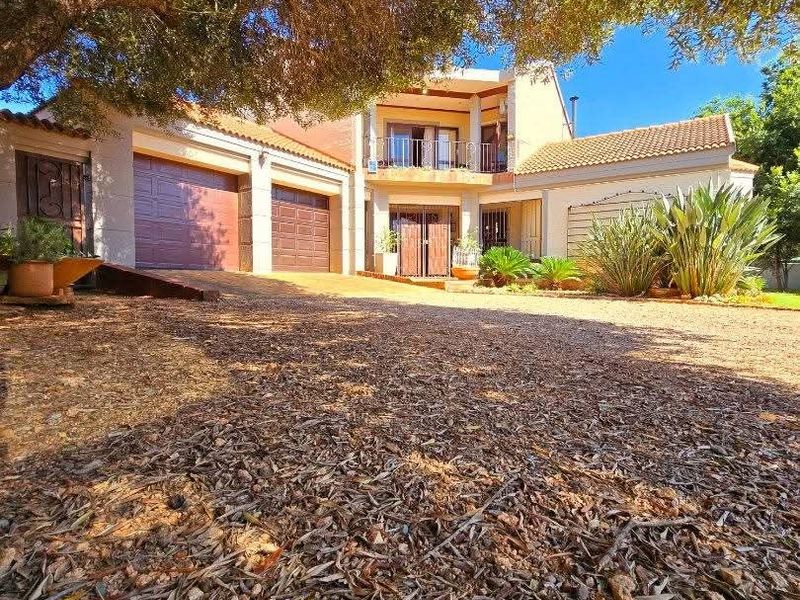 Front elevation of a multi-level residential property featuring a double garage, balcony, and paved driveway under mature trees.