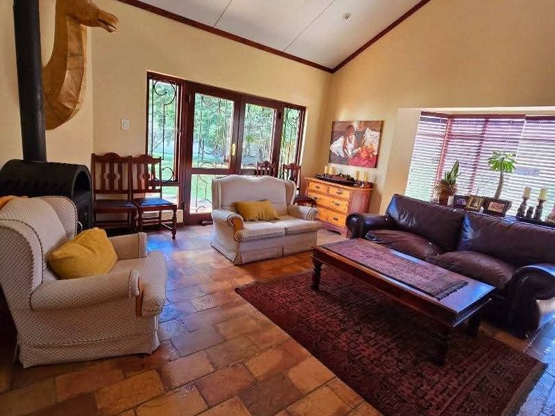 Spacious living room featuring terracotta tile flooring, a vaulted ceiling, a wood-burning fireplace, and large windows providing ample natural light.