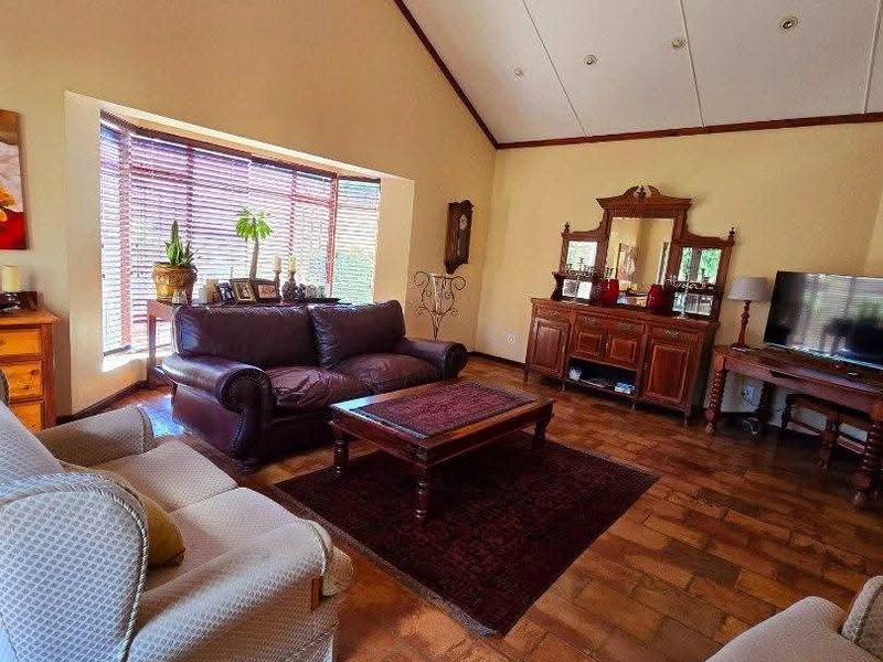 Spacious living room featuring a high vaulted ceiling with exposed timber beams, terracotta tile flooring, and a large bay window providing natural light.