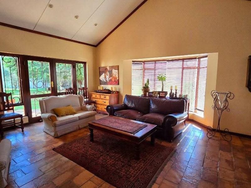 Spacious living room featuring vaulted ceilings with exposed timber beams, terracotta tile flooring, and a large bay window providing natural light.