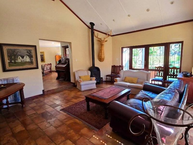 Spacious living room featuring vaulted ceilings with exposed timber beams, terracotta floor tiles, and a freestanding wood-burning fireplace with access to the garden.