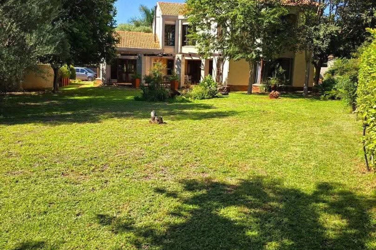 A spacious rear garden featuring a well-maintained lawn, mature trees, and a view of the multi-story residential building with a terracotta tiled roof.