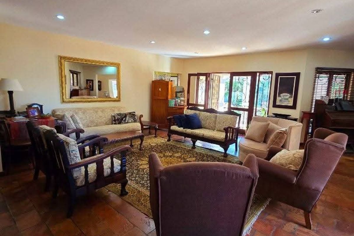 Spacious living room featuring traditional terracotta floor tiles, recessed downlighting, and large timber-framed french doors providing access to the outdoor area.