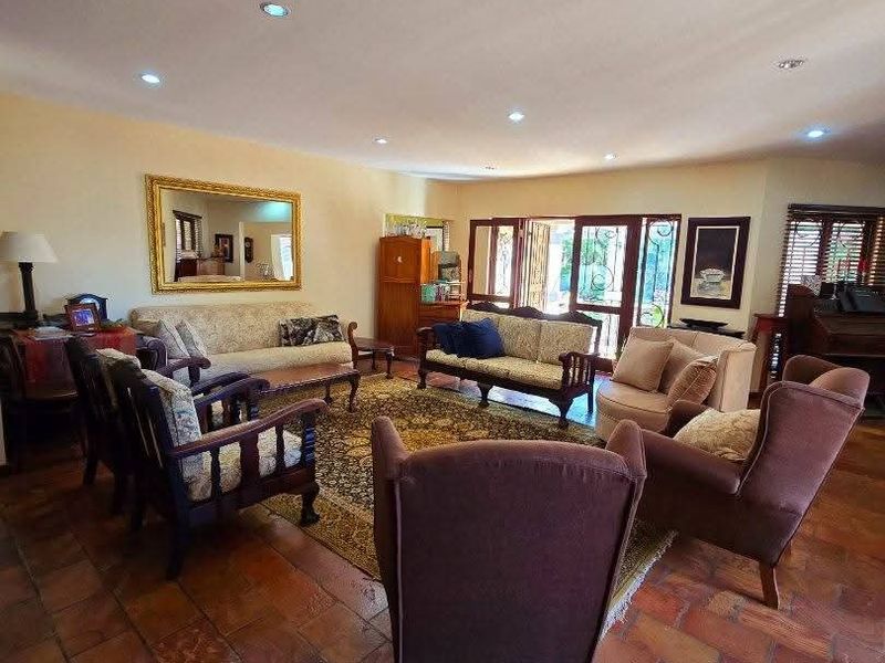 Spacious living room featuring traditional terracotta floor tiles, recessed downlighting, and large timber-framed french doors providing access to the outdoor area.