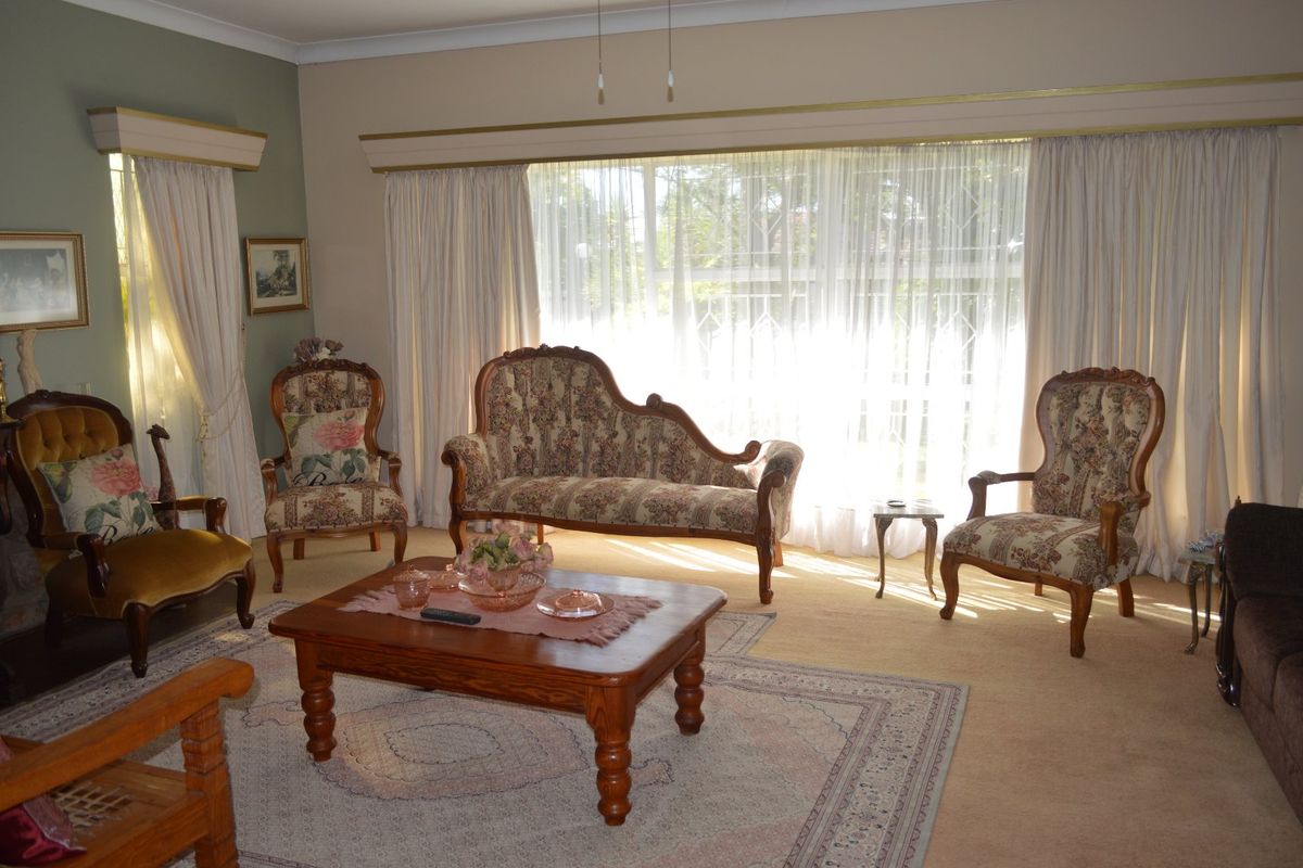 A spacious living room featuring large windows with security bars, neutral wall tones, and classic cornice detailing, offering a bright and comfortable living space.
