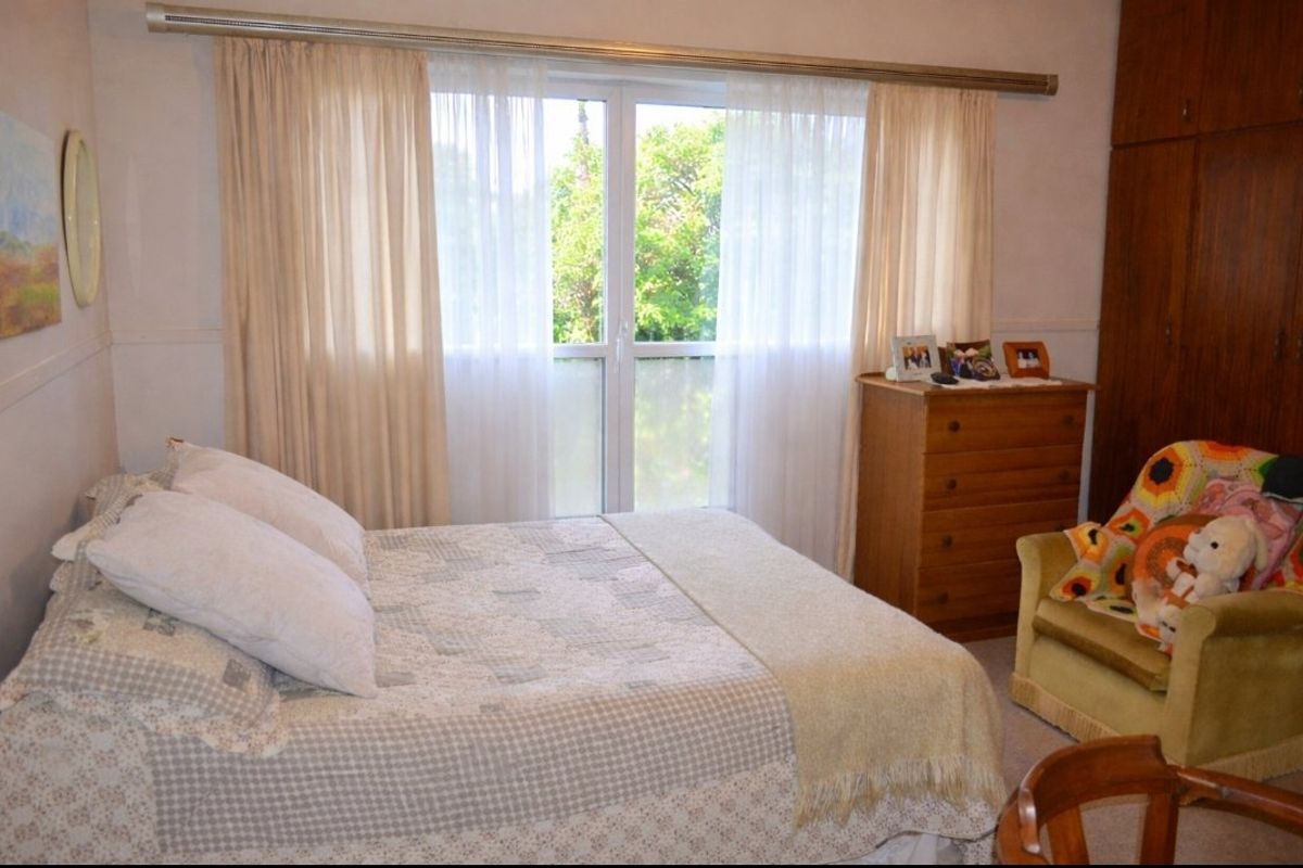 A bedroom featuring built-in wooden cupboards and a sliding glass door providing natural light and garden views.