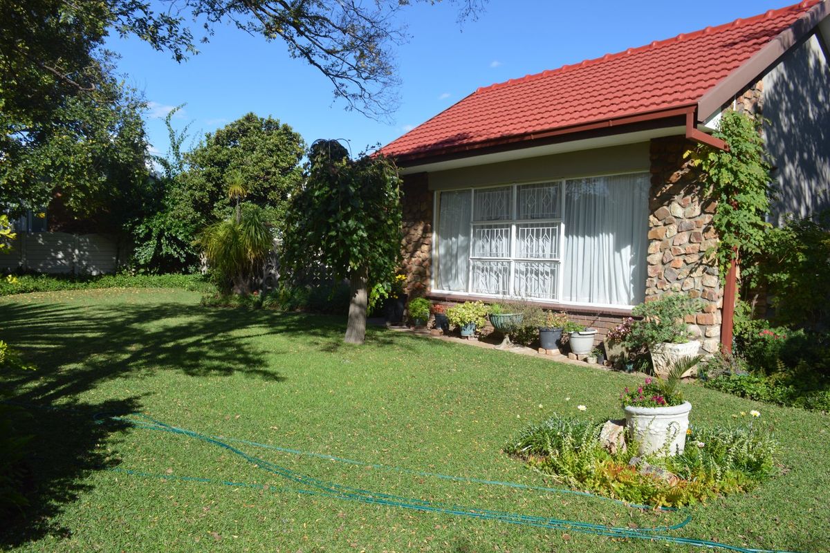 A well-maintained rear garden featuring a stone-clad exterior wall, tiled roof, and established lawn area.