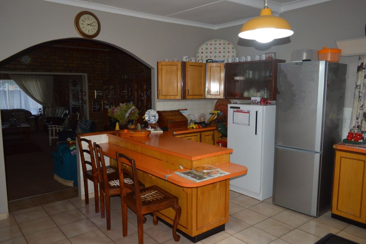 A dated kitchen featuring wooden cabinetry, a breakfast bar, and tiled flooring, with an open archway leading into the adjacent living area.