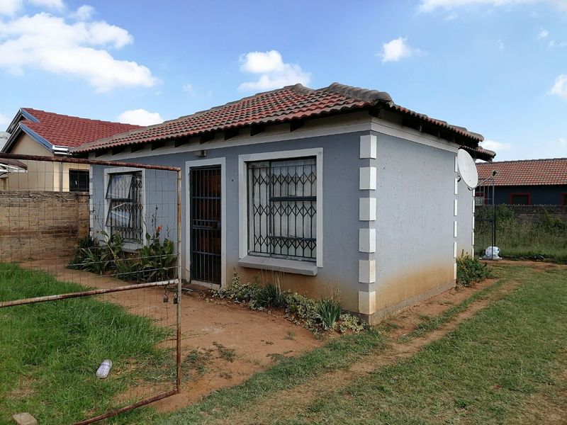 Rear view of a detached house featuring a tiled roof, security bars on windows, and a security gate, set within an unpaved garden area.
