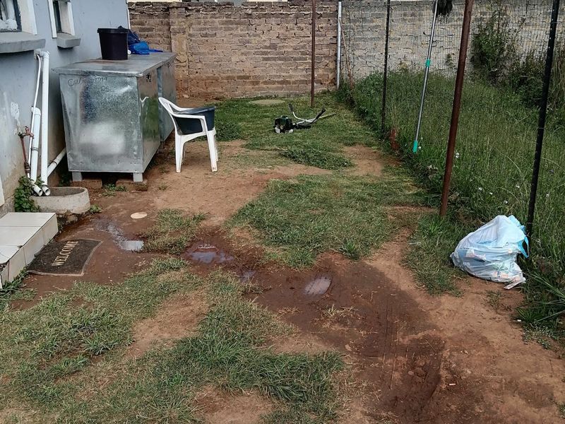 Rear yard area featuring a brick boundary wall, wire fencing, and a metal washing line, requiring landscaping and drainage improvements.