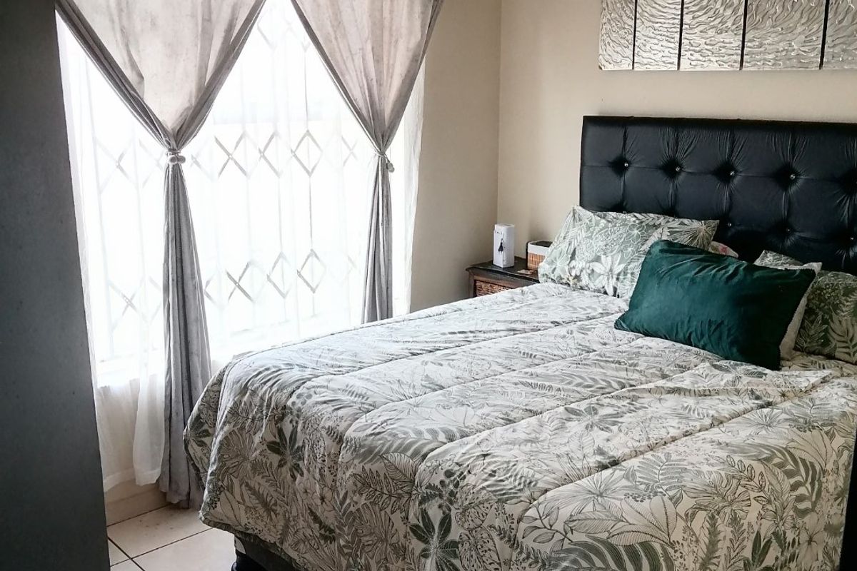 A functional bedroom featuring tiled flooring and a window fitted with a security gate, providing a practical and secure sleeping space.