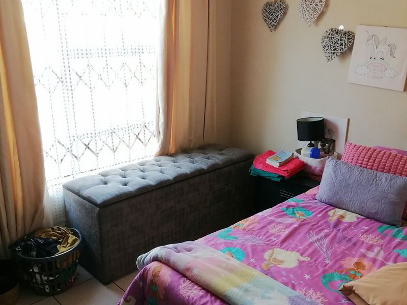 A functional bedroom featuring tiled flooring and a window fitted with a security gate, providing natural light and basic security.