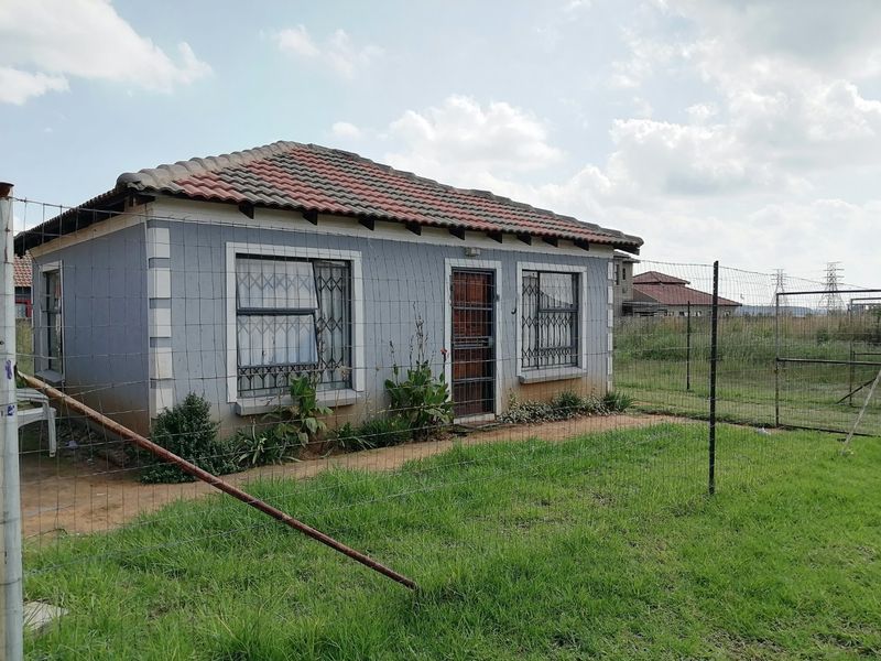 A detached single-story house featuring a tiled roof and security gates, set within a fenced yard area.