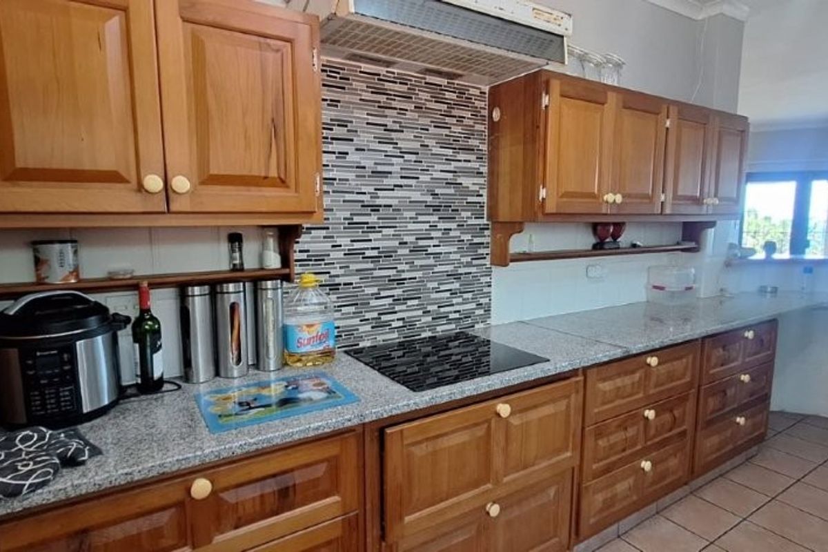 A functional kitchen featuring traditional wooden cabinetry, granite countertops, a modern electric hob, and a decorative tiled backsplash.