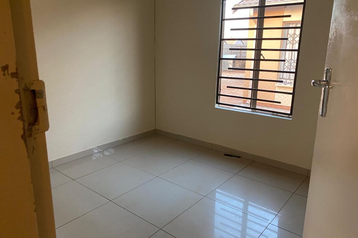 A clean, empty bedroom featuring neutral tiled flooring and a window fitted with security bars.