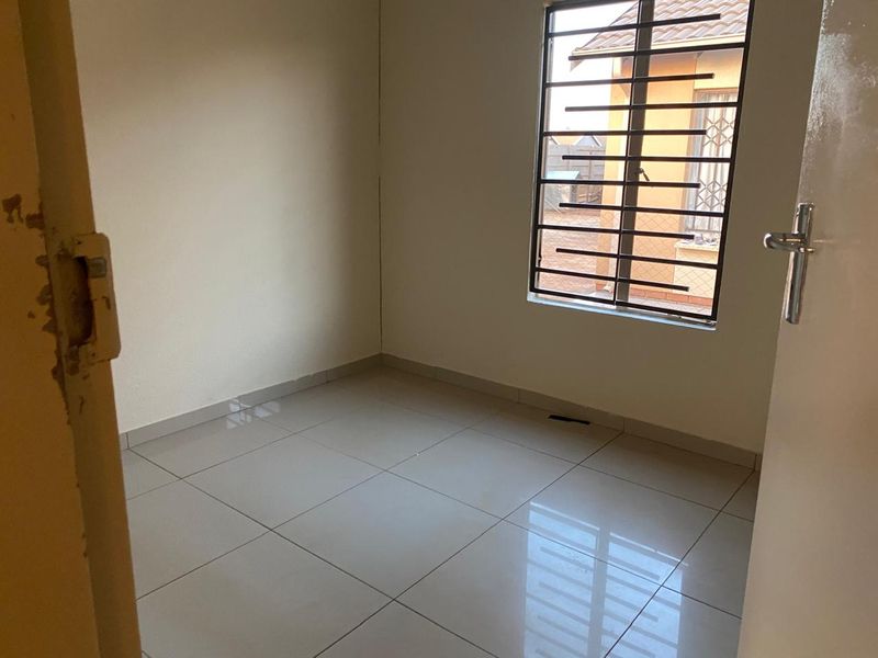 A clean, empty bedroom featuring neutral tiled flooring and a window fitted with security bars.
