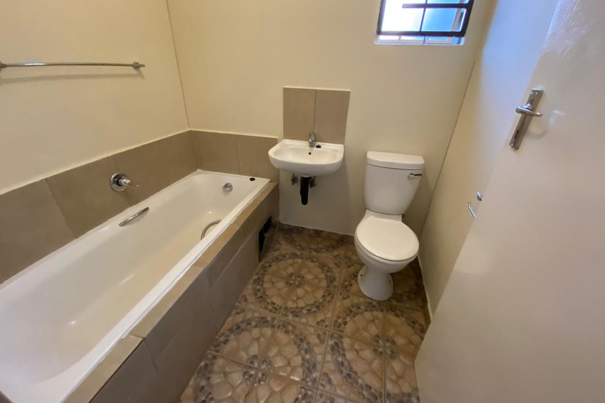 A functional bathroom featuring a bathtub, wall-mounted basin, and toilet with tiled flooring and splashbacks.