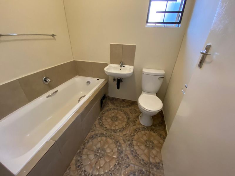 A functional bathroom featuring a bathtub, wall-mounted basin, and toilet with tiled flooring and splashbacks.
