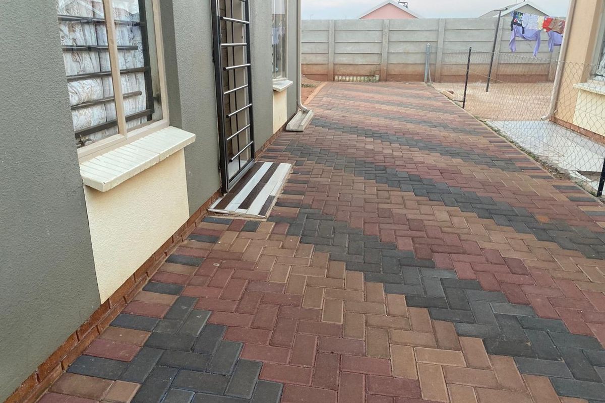 A well-maintained rear exterior area featuring patterned brick paving, a security gate, and a secure perimeter boundary wall.