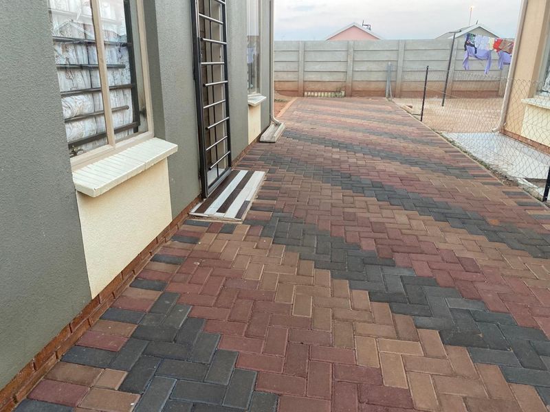 A well-maintained rear exterior area featuring patterned brick paving, a security gate, and a secure perimeter boundary wall.