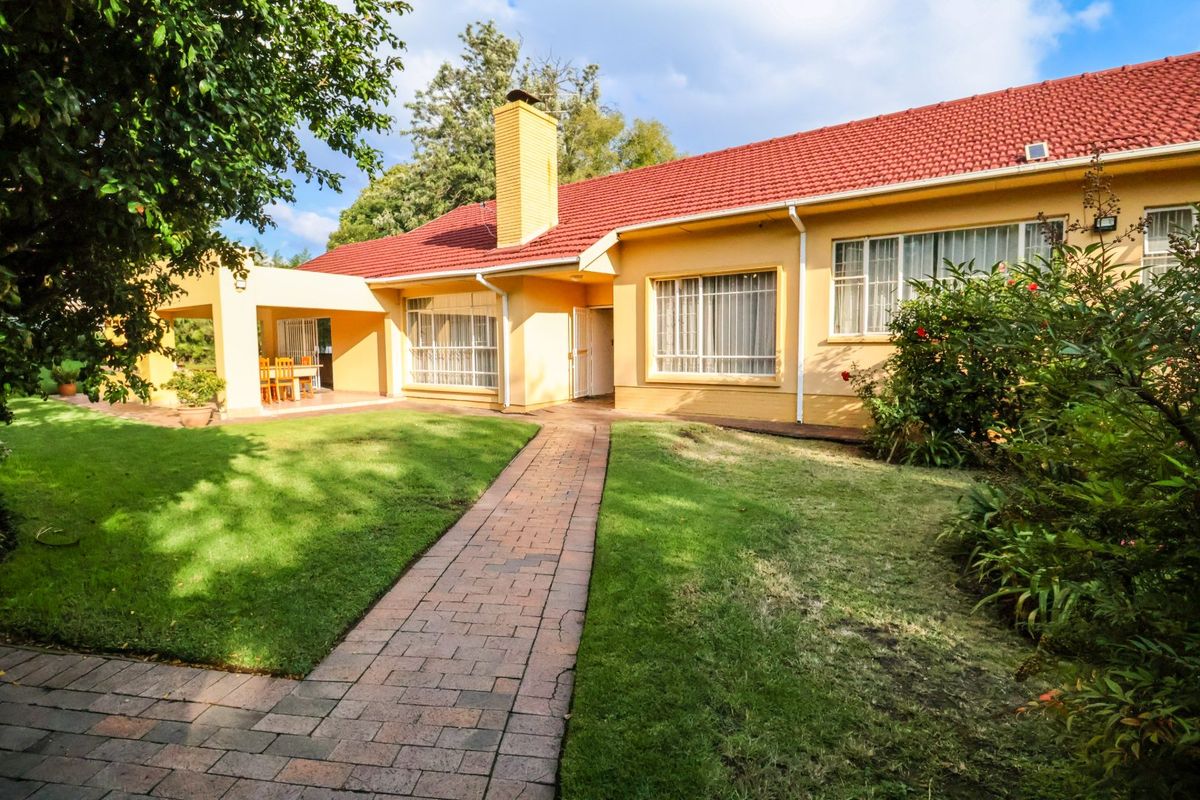 A well-maintained rear exterior view of the house featuring a red tiled roof, yellow facade, paved walkway, and a covered patio area.