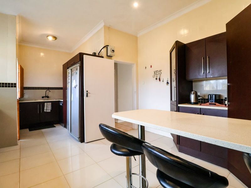 A functional kitchen featuring dark cabinetry, stone countertops, a breakfast bar, and tiled flooring, offering a practical layout for daily meal preparation.