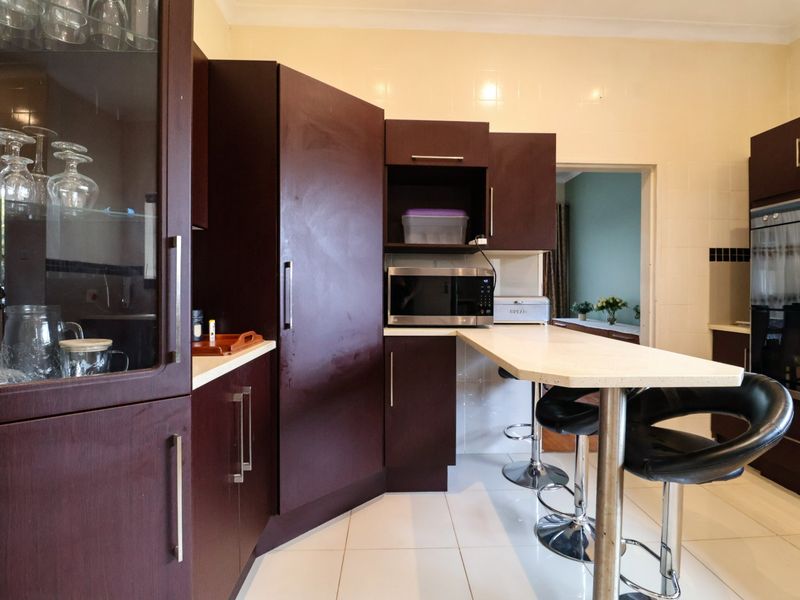 A functional kitchen featuring dark wood cabinetry, a breakfast bar, built-in oven, and microwave, complemented by tiled flooring and splashbacks.