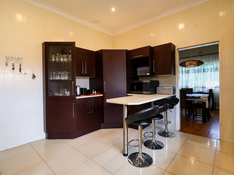 A functional kitchen featuring dark wood cabinetry, a breakfast bar, and tiled finishes, with a view into the adjacent dining area.