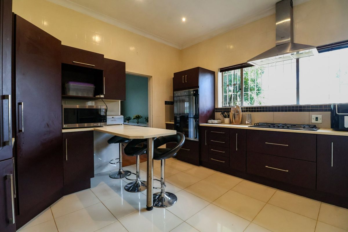 A functional kitchen featuring dark wood cabinetry, built-in oven, gas hob, stainless steel extractor fan, and a convenient breakfast bar with tiled flooring.