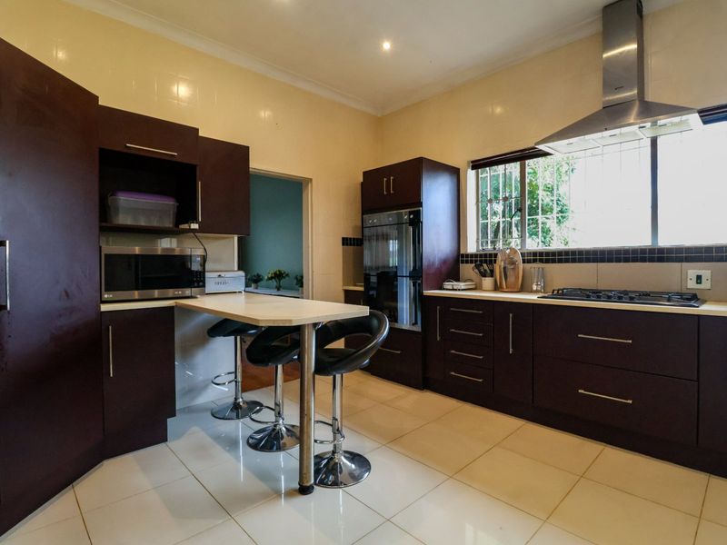 A functional kitchen featuring dark wood cabinetry, built-in oven, gas hob, stainless steel extractor fan, and a convenient breakfast bar with tiled flooring.