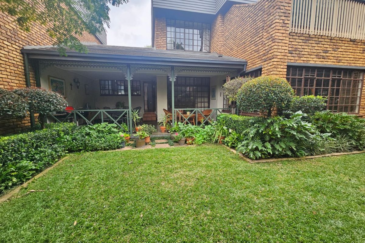 Rear view of a townhouse featuring a covered patio with timber lattice detailing, overlooking a well-maintained private garden and brick exterior facade.