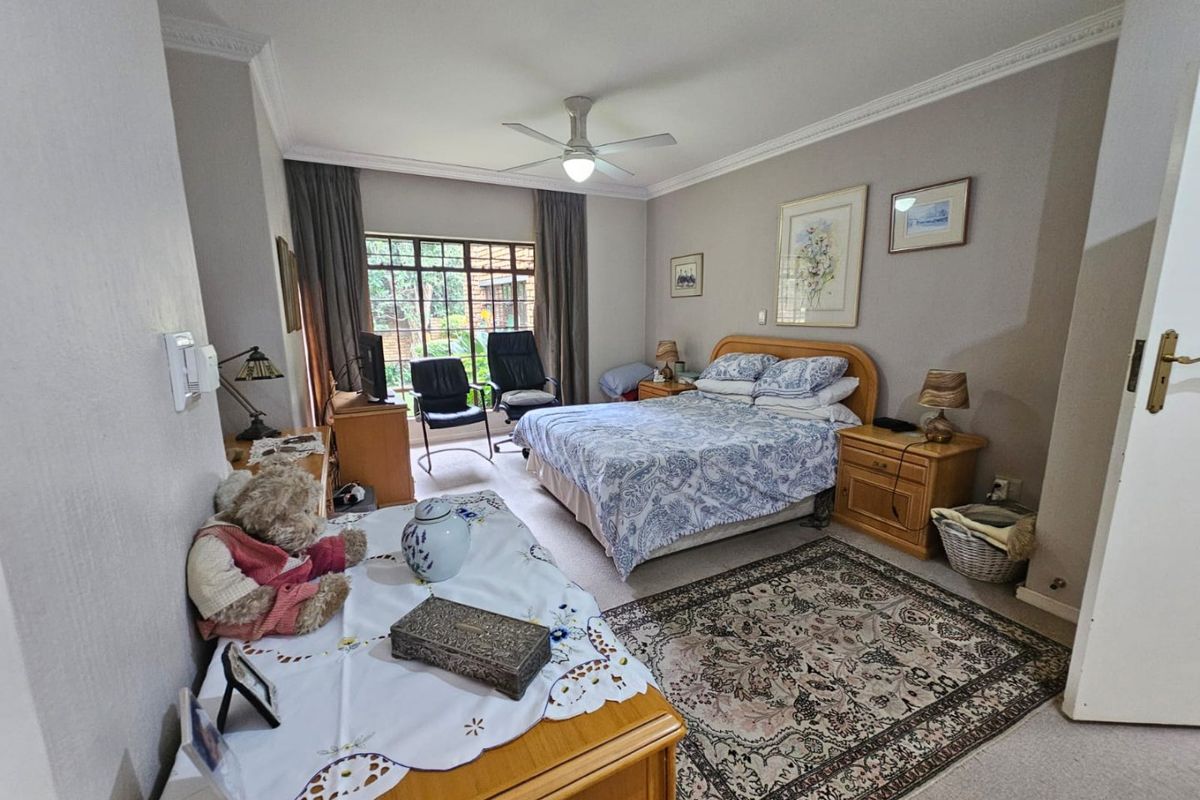 A spacious bedroom featuring crown molding, a ceiling fan, and large windows that provide natural light and a view of the garden.