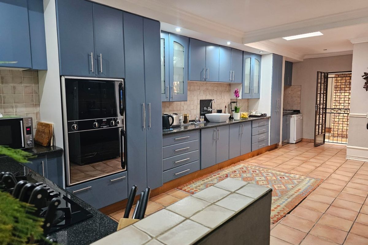 Spacious kitchen featuring blue cabinetry, granite countertops, built-in oven, and tiled flooring, with direct access to an outdoor area through a security gate.