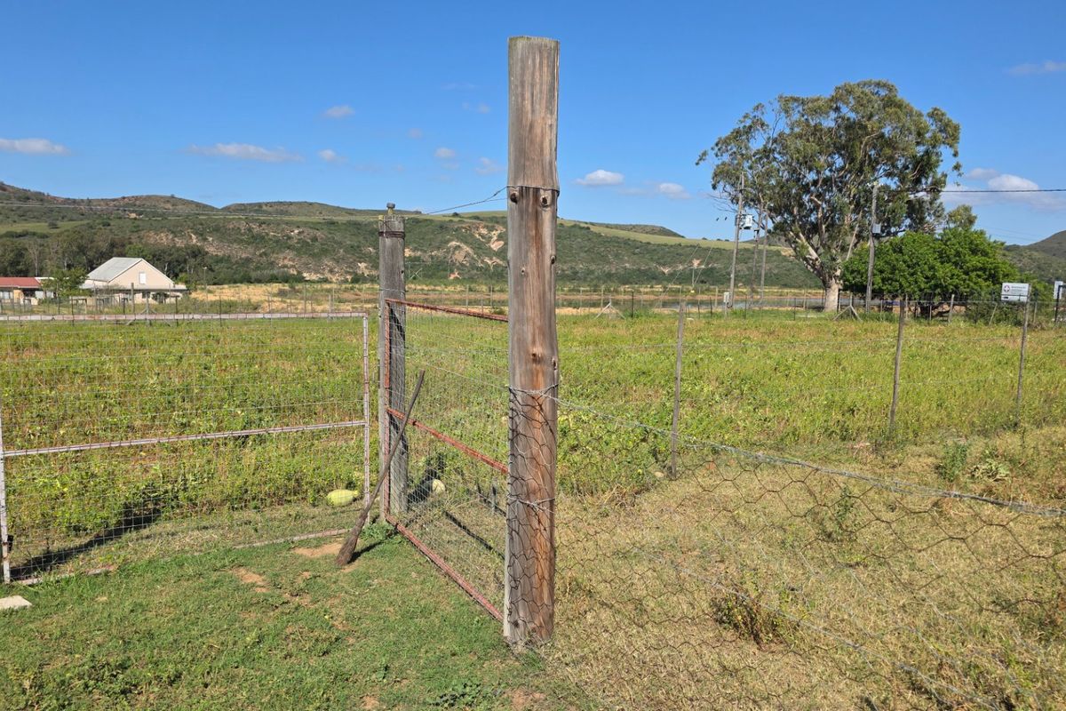 A view of a vacant residential plot featuring basic wire fencing and timber posts, set against a rural landscape backdrop.