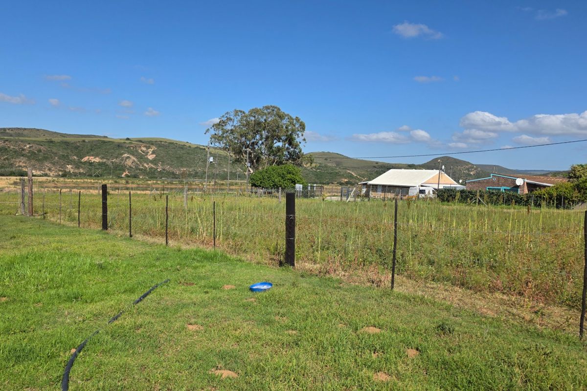 A view of a vacant residential plot featuring open grassy terrain, perimeter wire fencing, and scenic mountain views in the background.
