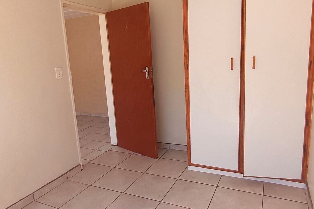 An empty bedroom featuring tiled flooring and built-in cupboards, providing a neutral space ready for personalization.