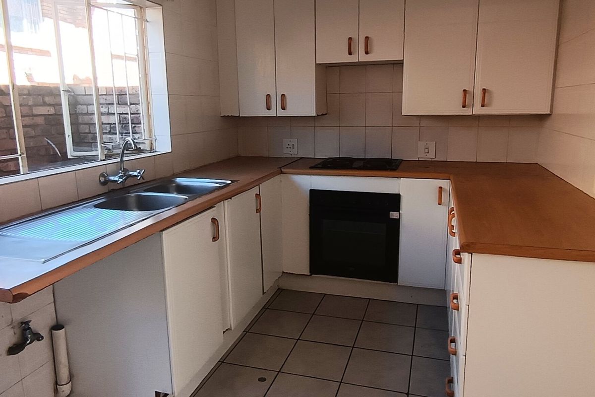 A functional kitchen featuring built-in cabinetry, laminate countertops, a stainless steel double sink, and a built-in oven with an electric hob.