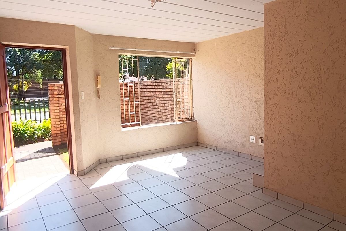 An empty living room featuring tiled flooring, textured walls, and a timber entrance door with natural light from a large window.