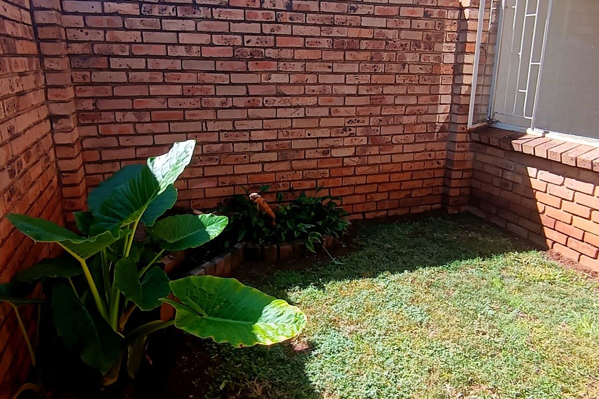 A private rear courtyard area featuring face brick walls, a small lawn, and a built-in brick planter.