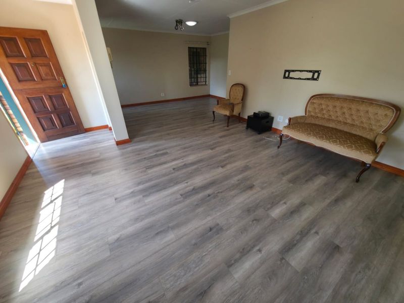 Spacious living area featuring modern laminate flooring, neutral walls, and a solid wooden entrance door.