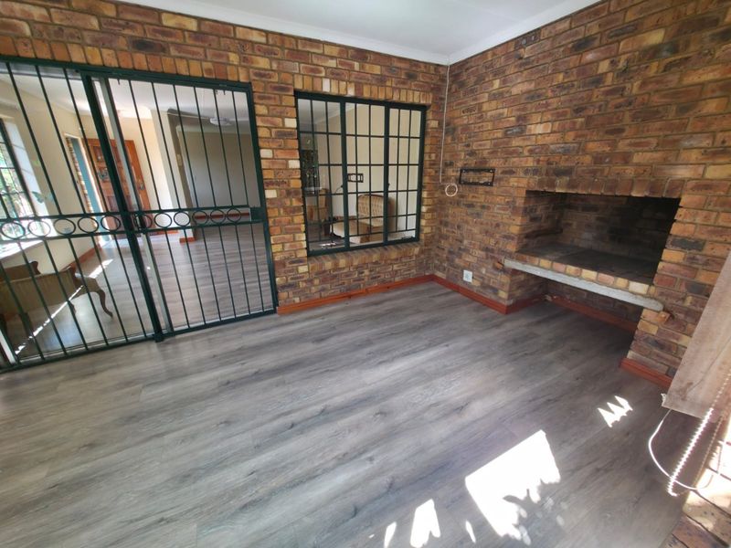 Enclosed patio area featuring exposed brick walls, a built-in brick fireplace, and modern laminate flooring, secured with metal security gates and window bars.