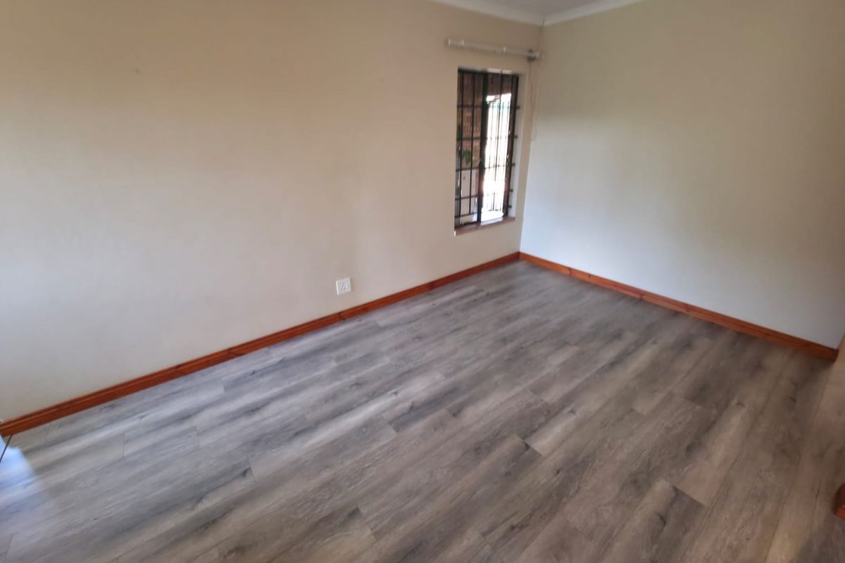 A clean, empty bedroom featuring modern grey laminate flooring, timber skirting boards, and a window fitted with security bars.