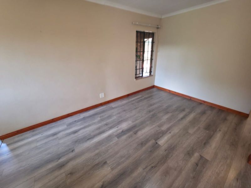 A clean, empty bedroom featuring modern grey laminate flooring, timber skirting boards, and a window fitted with security bars.