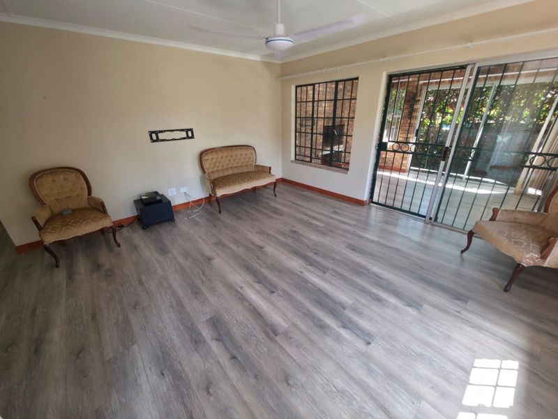 Spacious living room featuring modern laminate flooring, a ceiling fan, and large sliding glass doors with security gates leading to the outdoor area.