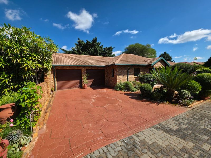 Front view of a brick house featuring a double garage, tiled roof, and a paved driveway surrounded by a well-maintained garden.