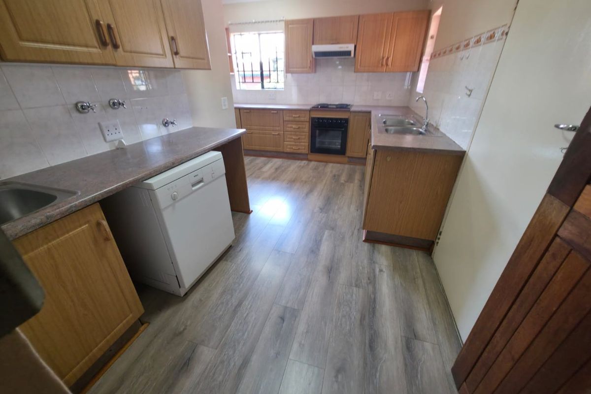 Functional kitchen featuring wood-finish cabinetry, laminate countertops, double basin sink, built-in oven with extractor fan, and modern wood-look laminate flooring.