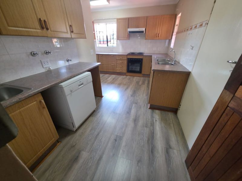 Functional kitchen featuring wood-finish cabinetry, laminate countertops, double basin sink, built-in oven with extractor fan, and modern wood-look laminate flooring.