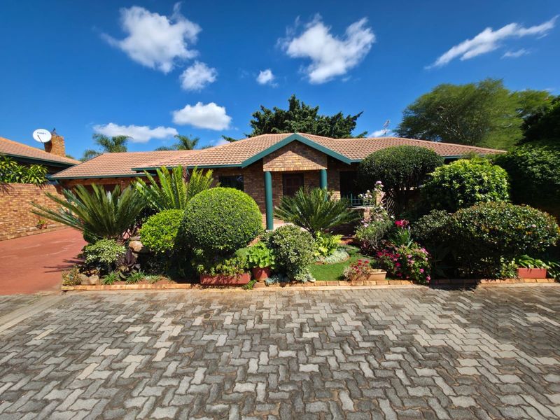 Front view of a single-story brick house featuring a tiled roof, covered entrance, and a well-maintained paved driveway with established garden landscaping.