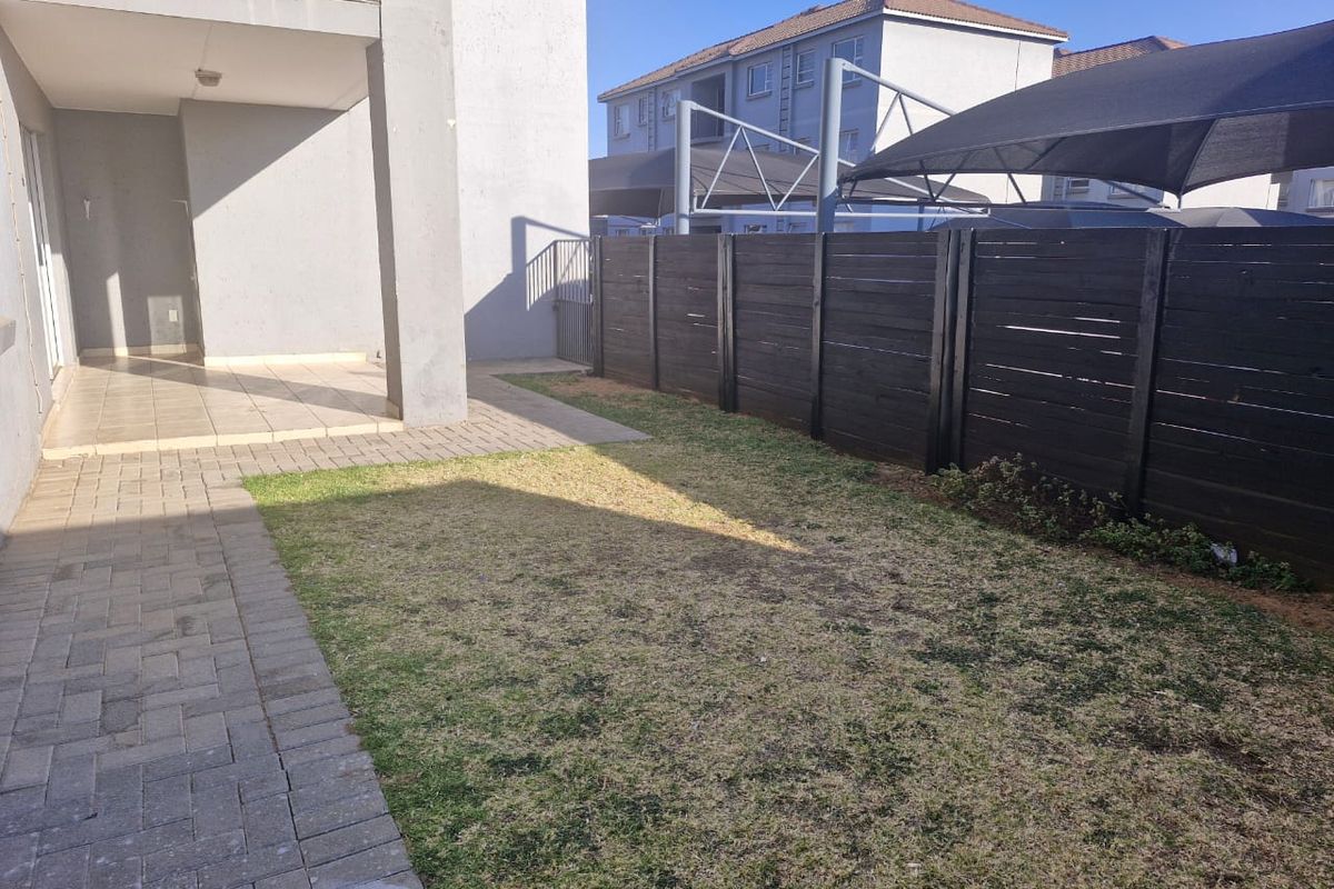 A private rear garden featuring a paved patio area, a small lawn, and a dark timber perimeter fence.