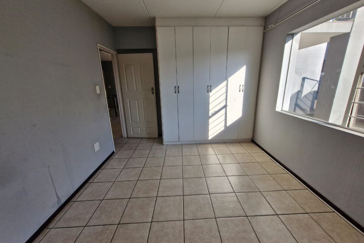 A vacant bedroom featuring neutral tiled flooring and built-in white cupboards, offering a clean canvas for personalization.